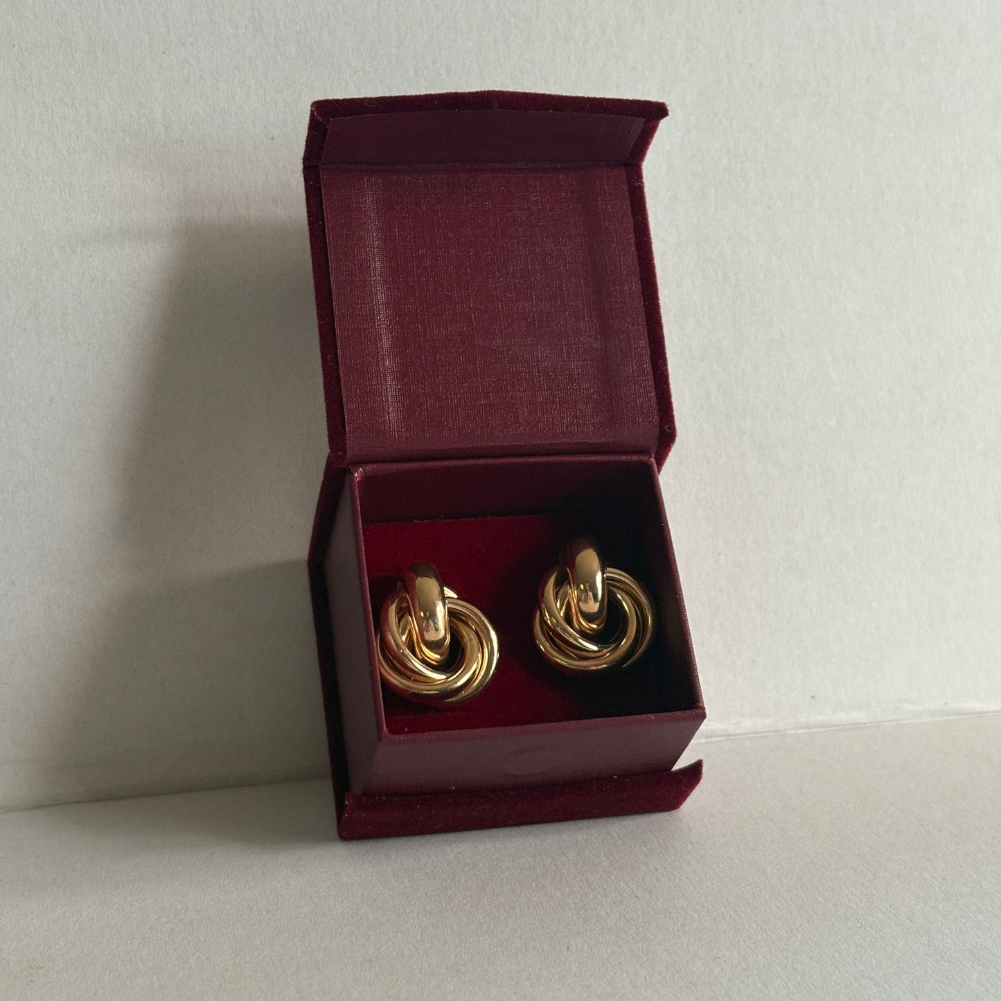 Gold earrings in a burgundy jewelry box on a light gray background