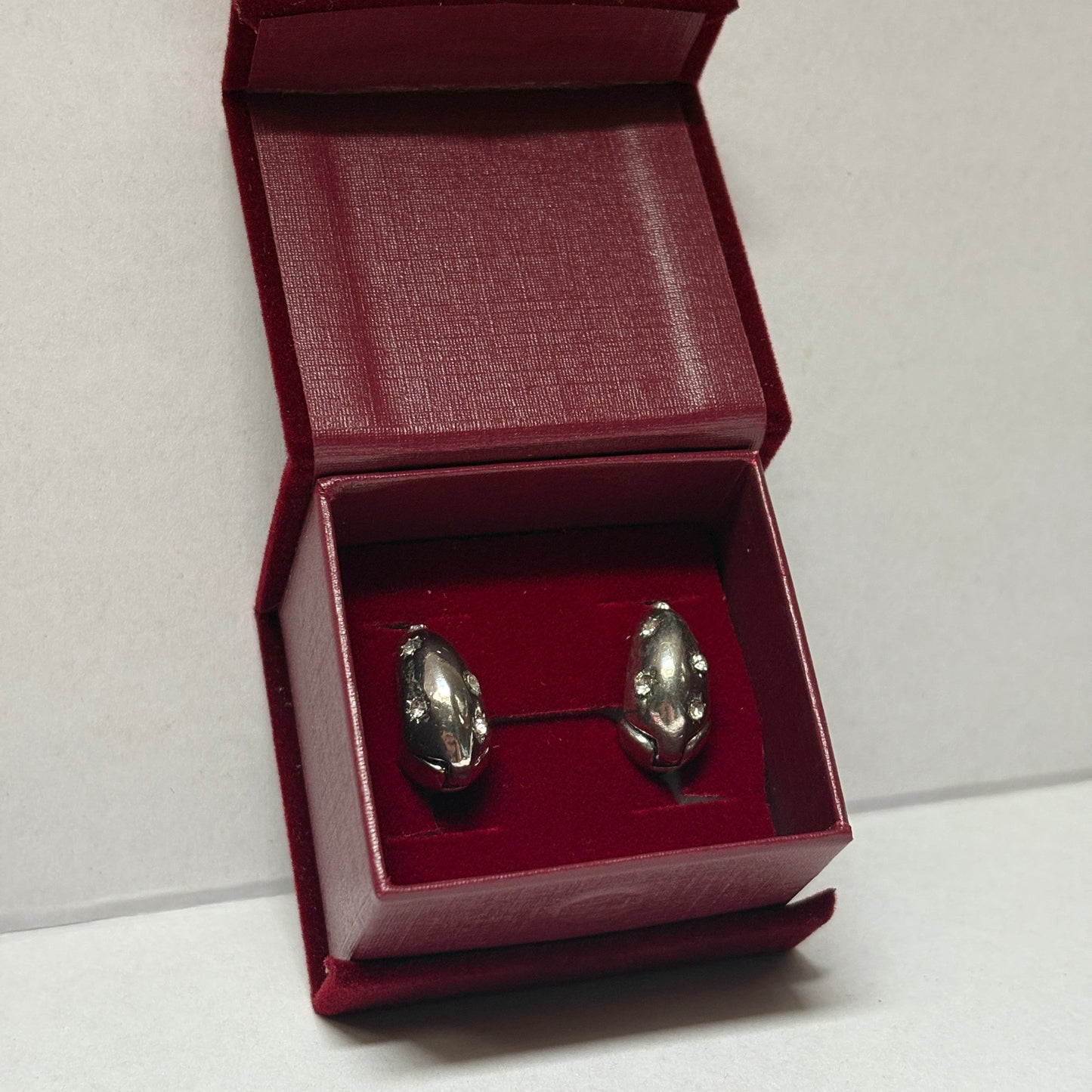 Two silver earrings in a red box on a white background