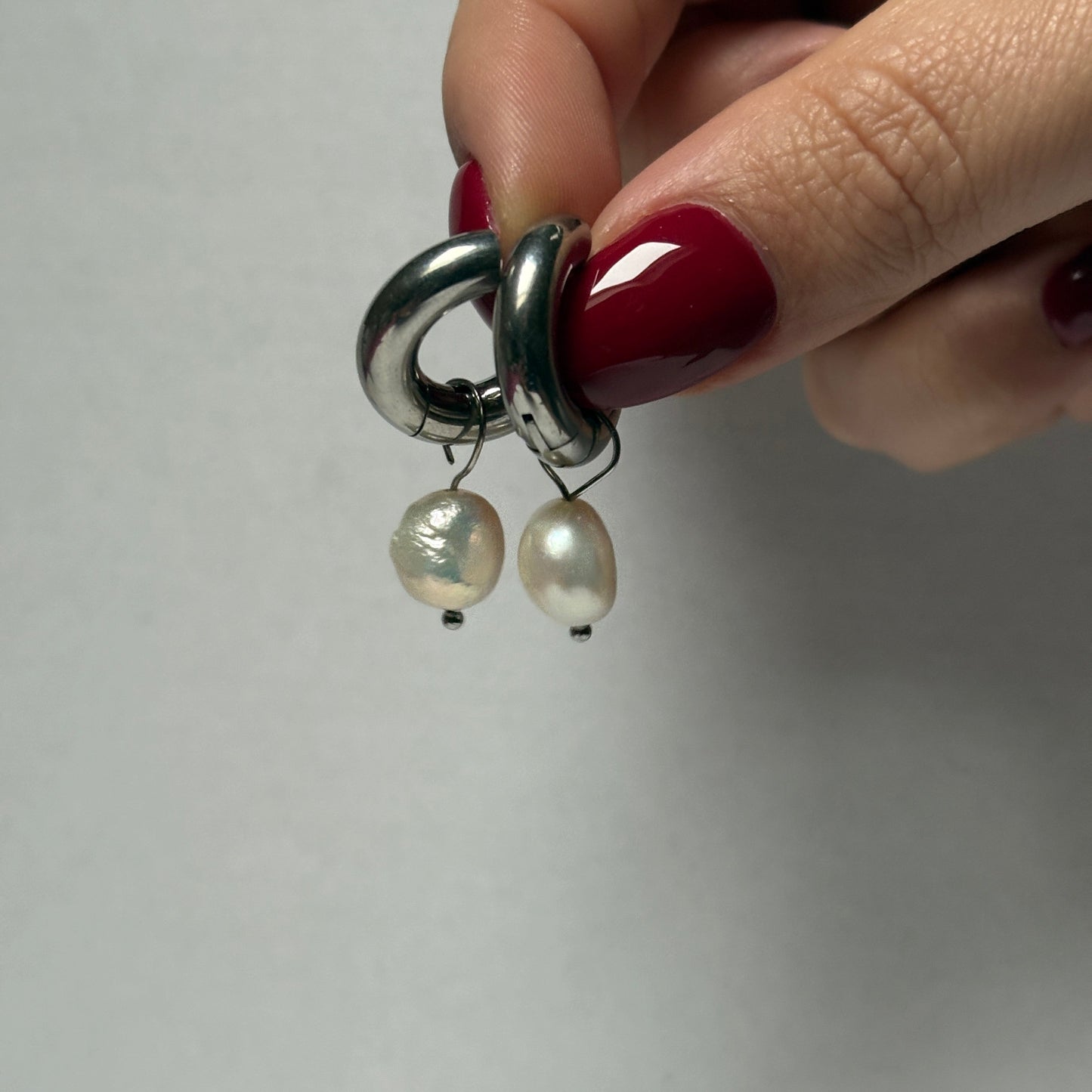 Hand holding a pair of pearl earrings against a plain background.