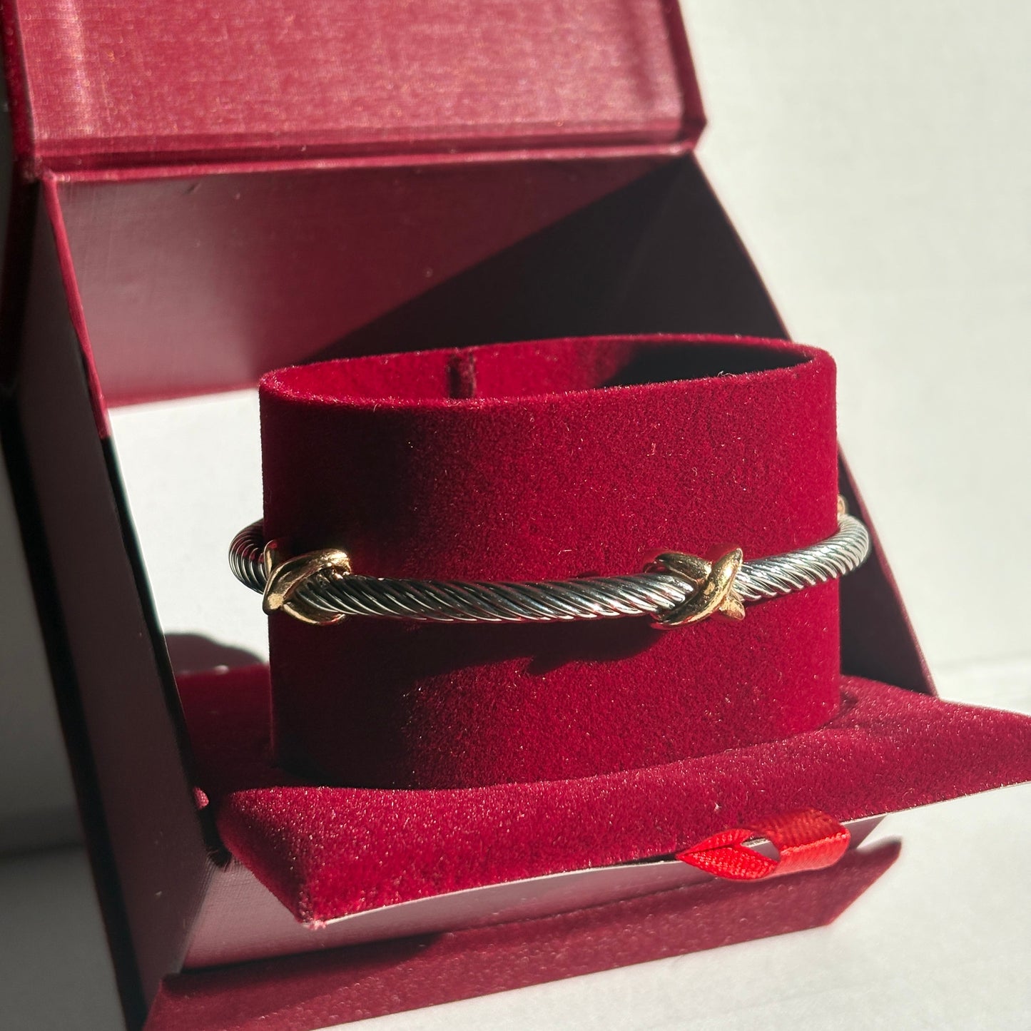 Gold bracelet on a red velvet cushion inside an open jewellery box.