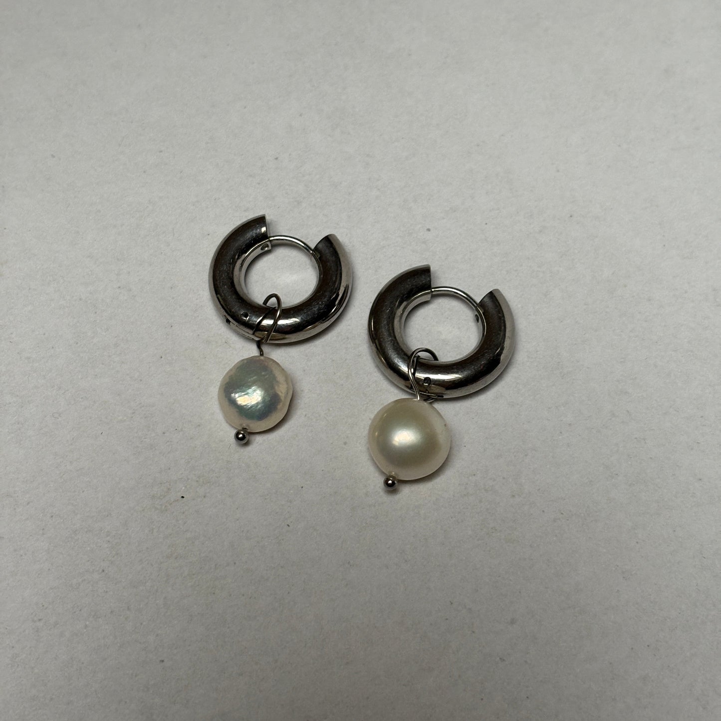 Pair of silver hoop earrings with pearl-like stones on a light gray background
