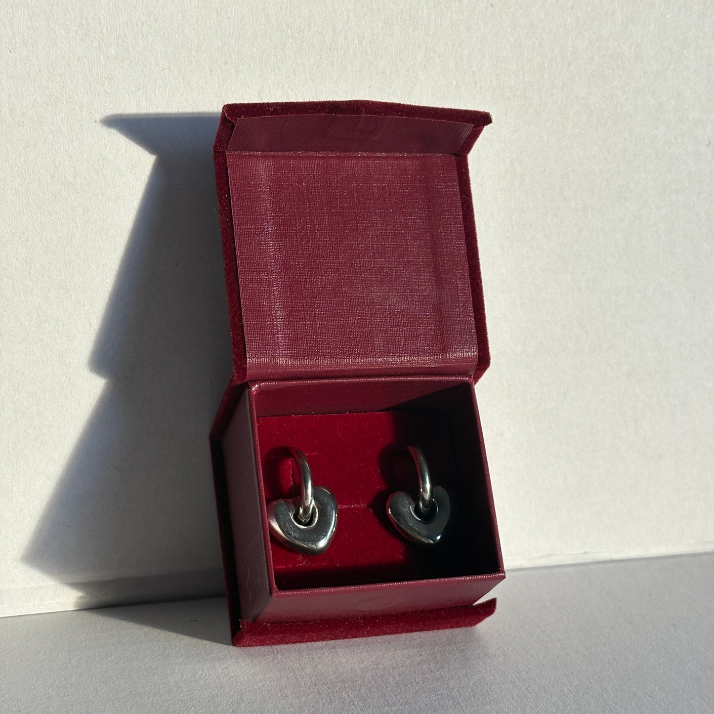 Red jewelry box with silver earrings on a light gray background.