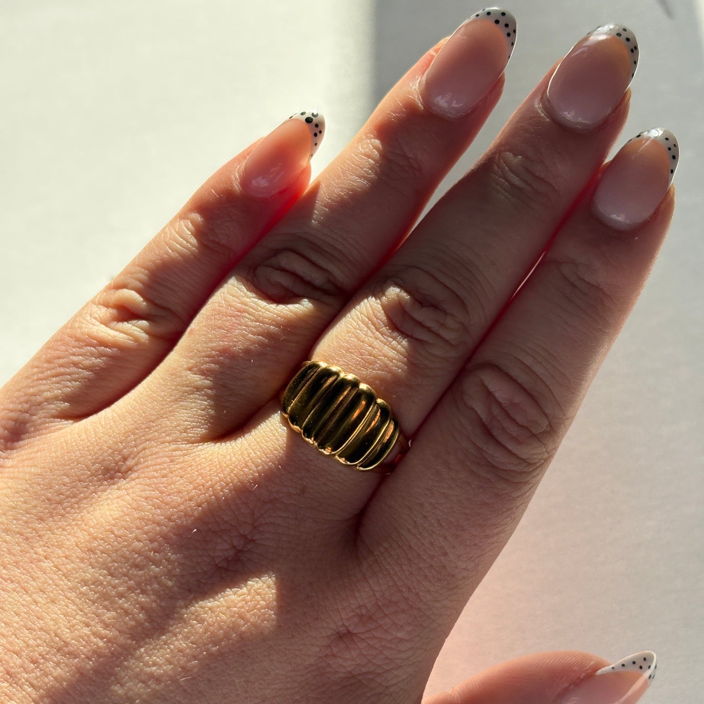 Hand wearing a gold ring with a textured band on a light background