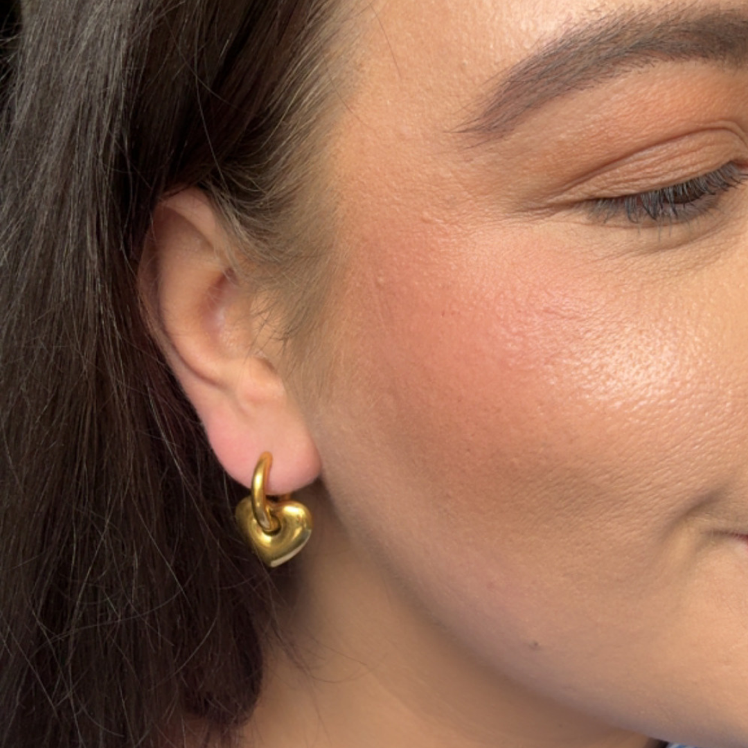 Close-up of a person wearing a gold heart-shaped earring.
