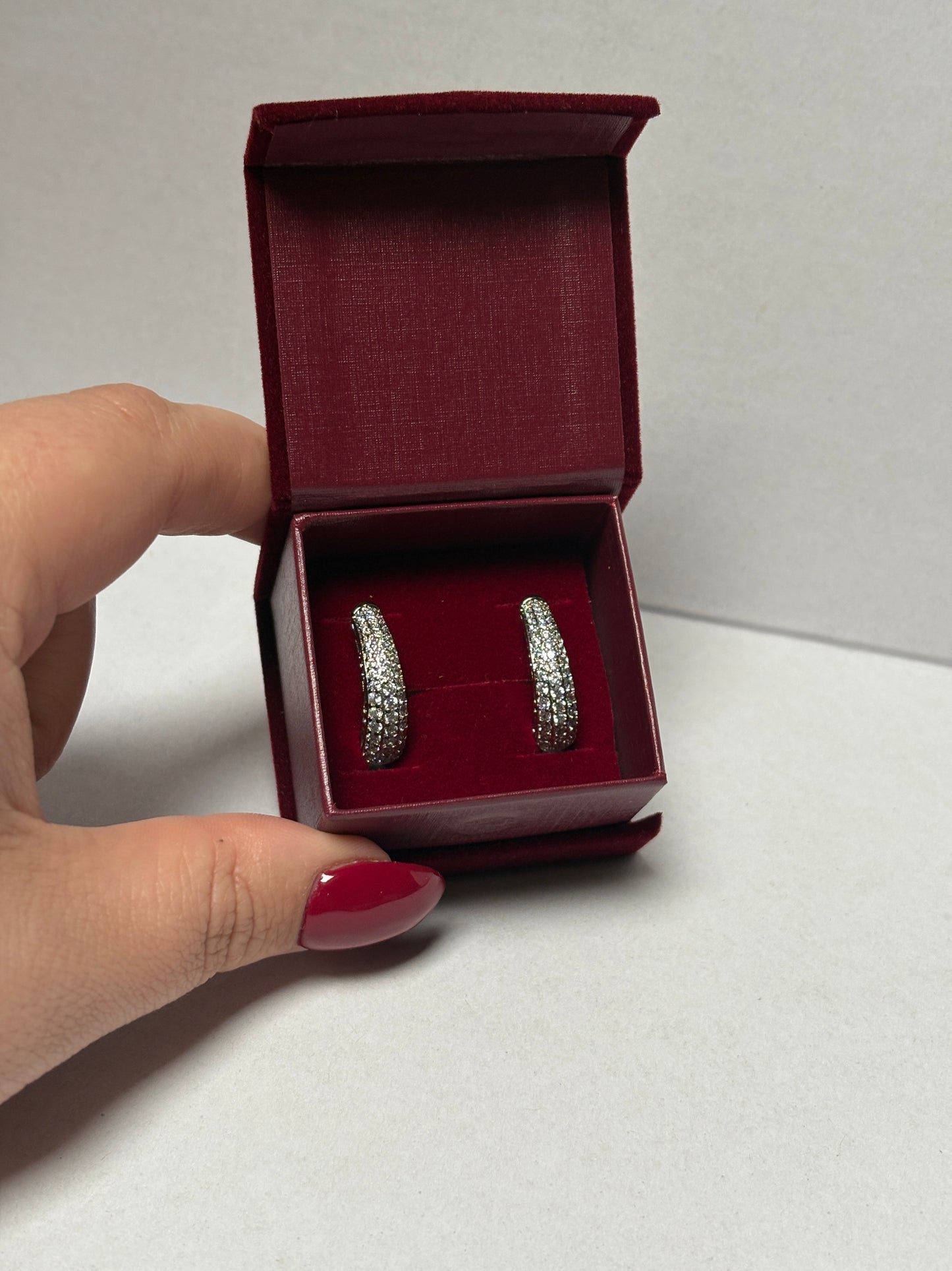 Two silver rings in a red box held by a hand with red nail polish on a light gray background.
