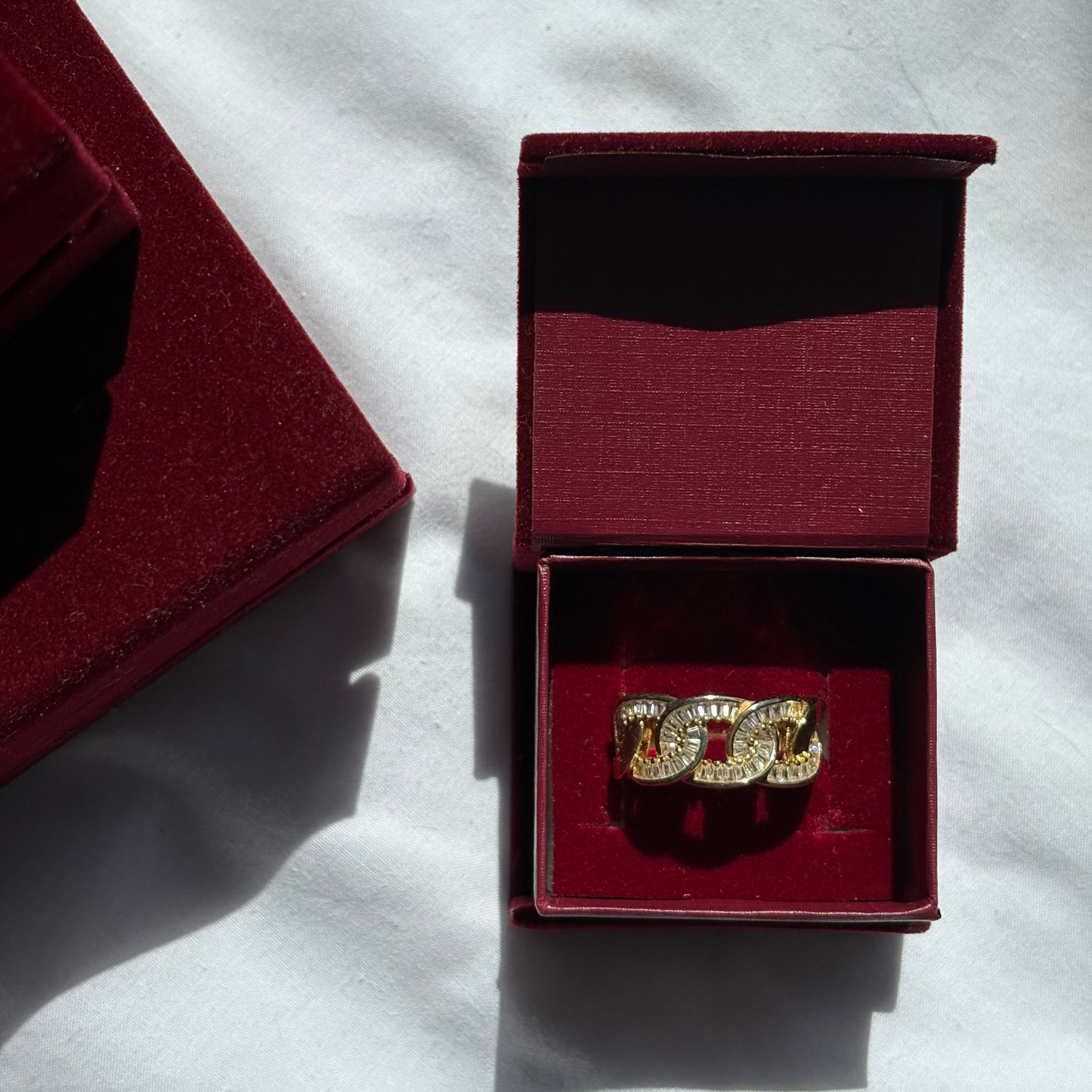 Gold ring with 'CC' design in a red jewelry box on a white surface