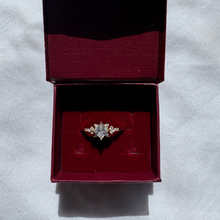 Gold ring with a central diamond and smaller stones on a light fabric background