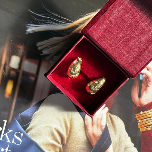 Gold earrings in a red box with a magazine in the background

