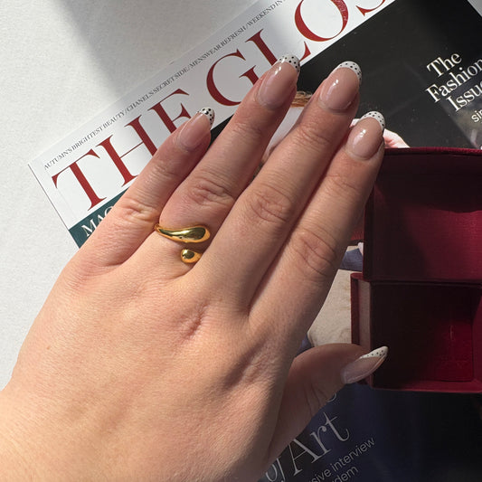 Hand wearing a gold ring with a magazine and book in the background

