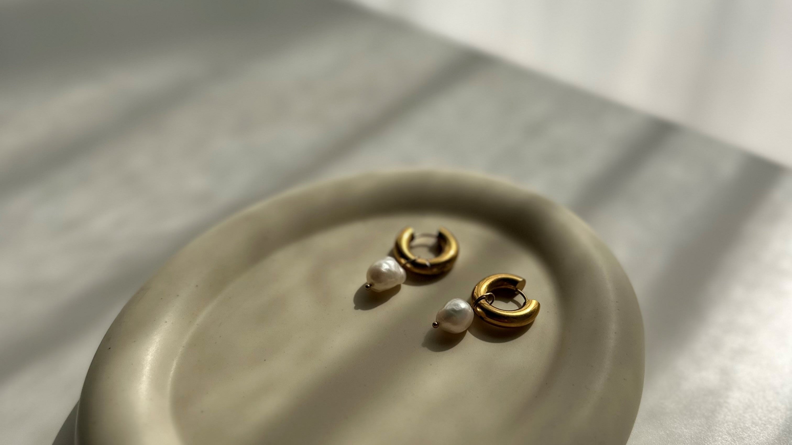 Pair of pearl and gold earrings on a beige plate with a neutral background

