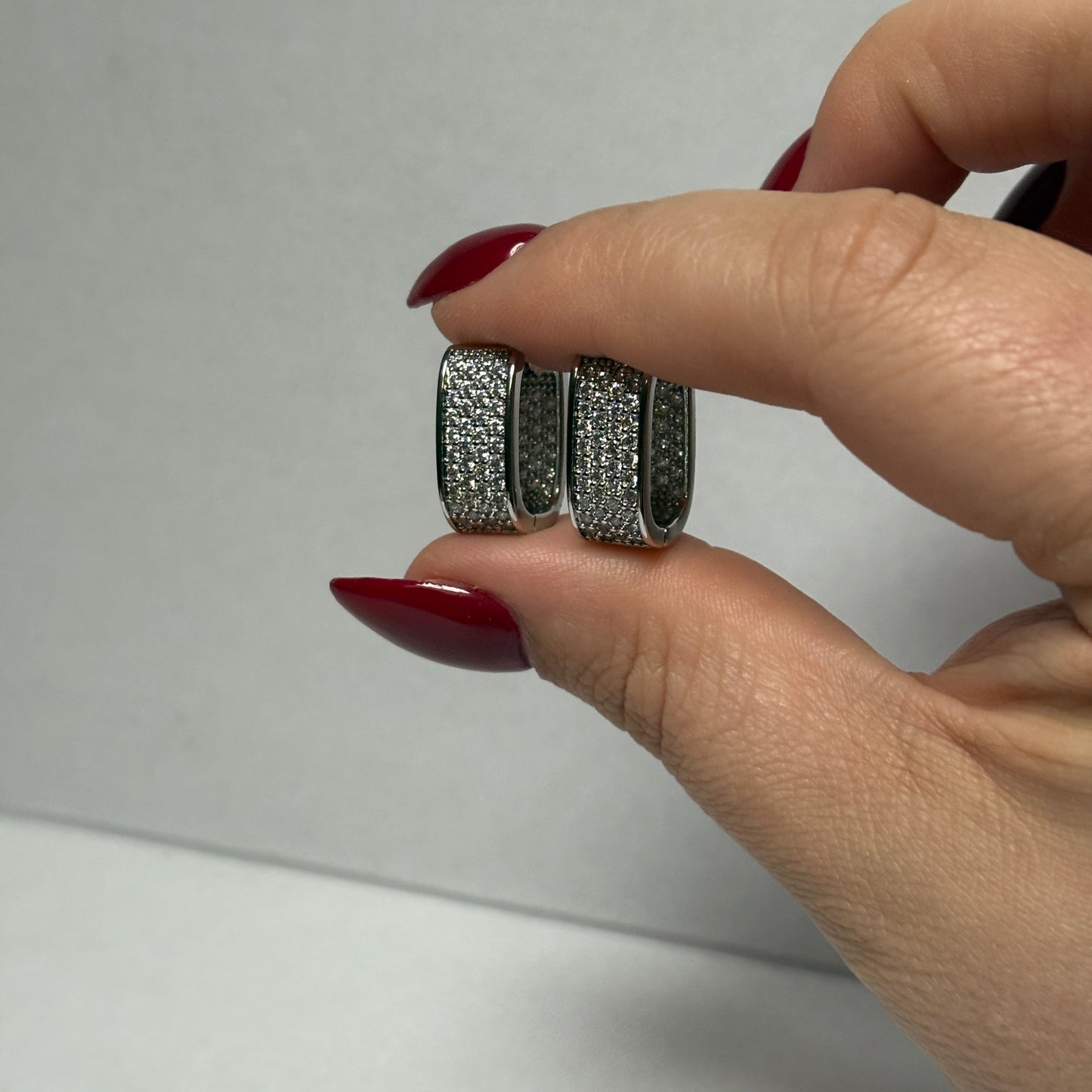 Hand holding two silver earrings with a plain background

