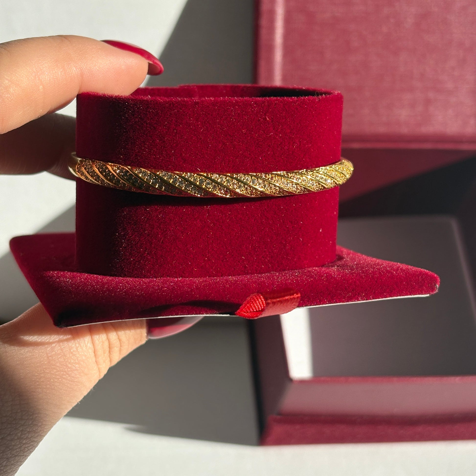 Gold bracelet on a red velvet stand held by a hand with a blurred background

