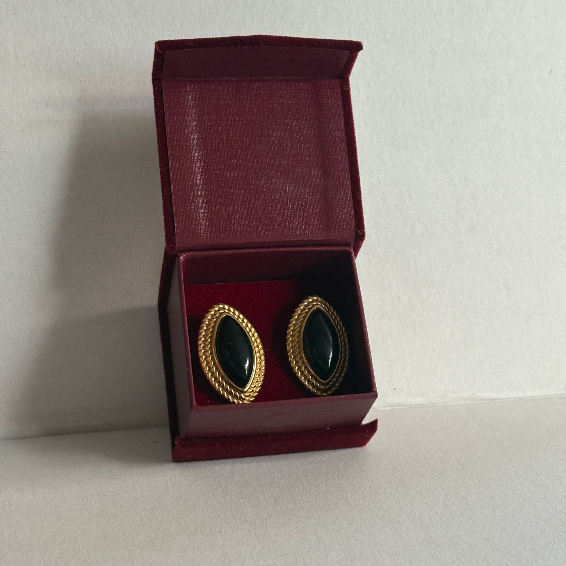 Pair of black earrings with gold accents in an open red jewelry box on a light gray background