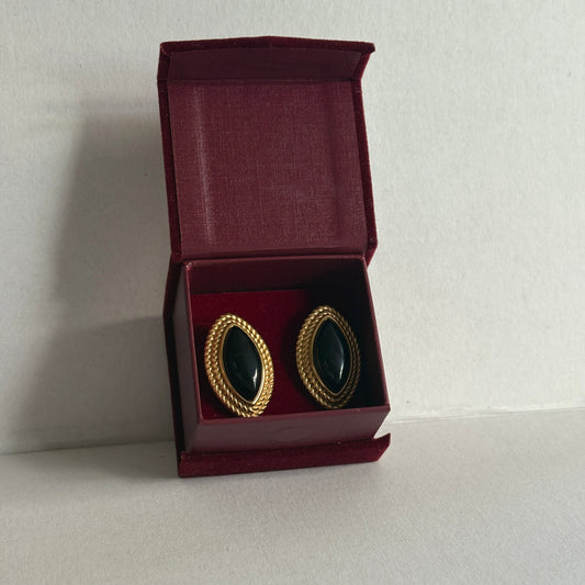 Pair of black earrings with gold accents in an open red jewelry box on a light gray background