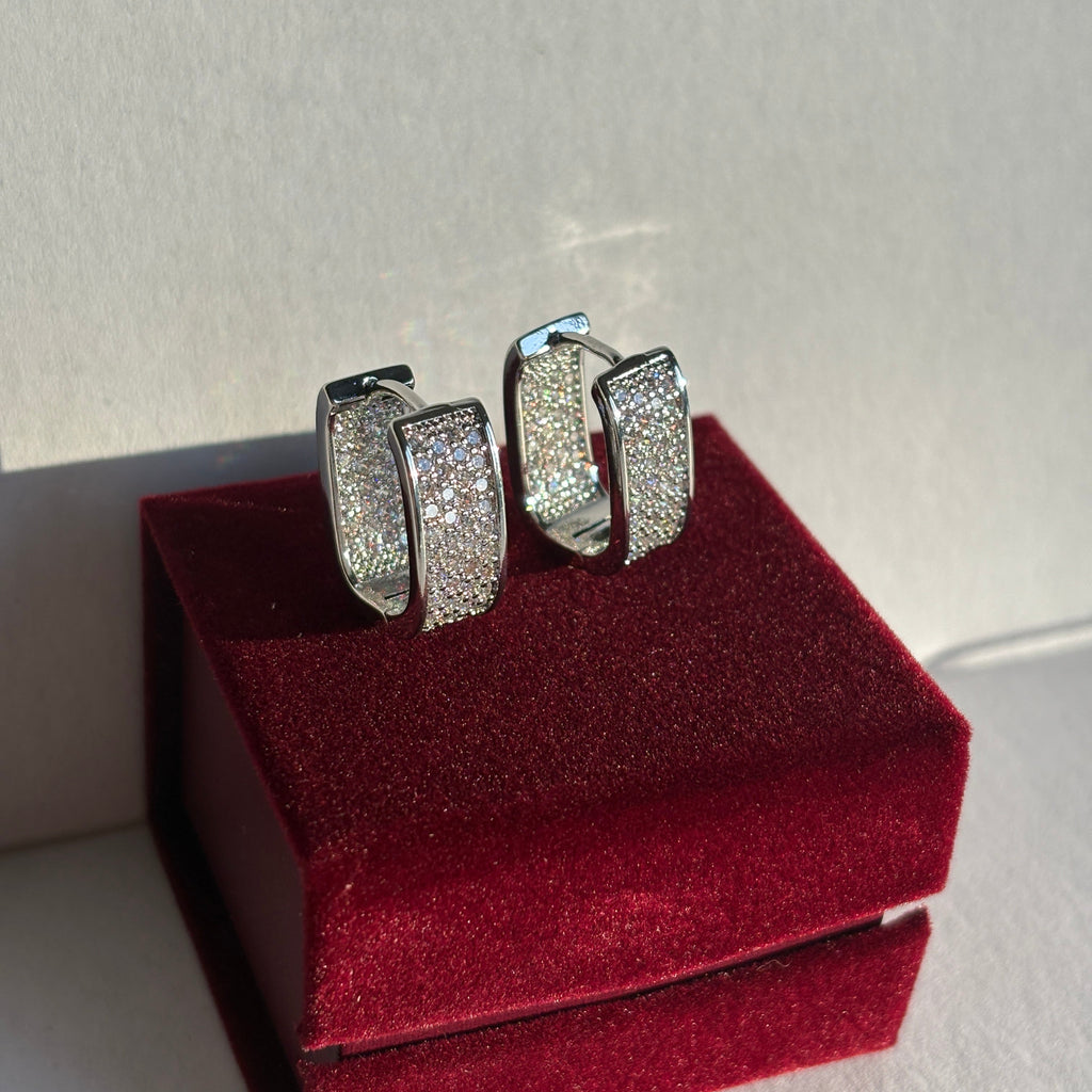 Silver earring with gemstones on a red velvet stand against a light background

