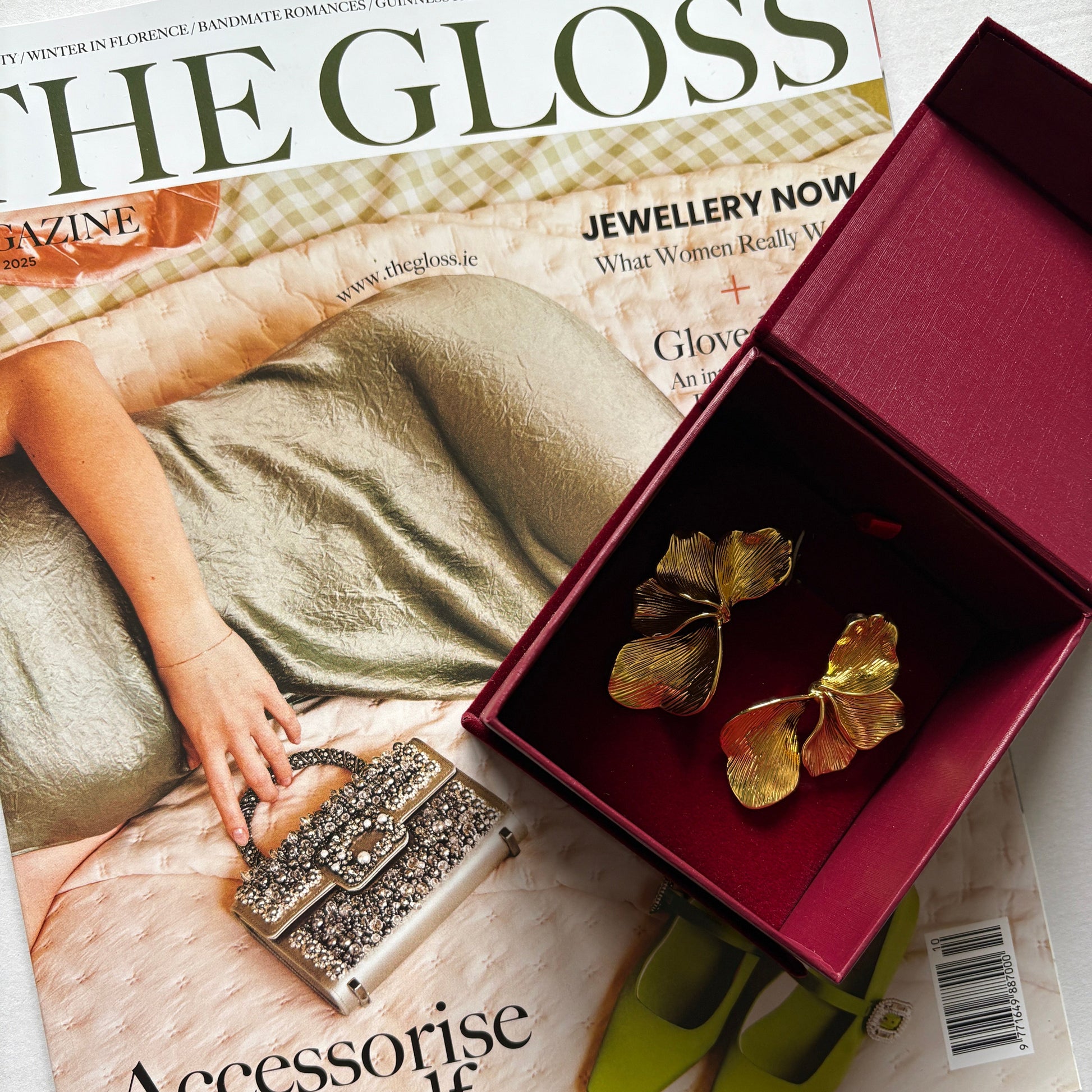 Jewelry box with gold flower earrings on a magazine titled 'The Gloss'.

