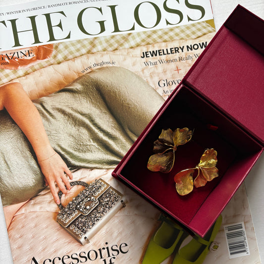 Jewelry box with gold flower earrings on a magazine titled 'The Gloss'.

