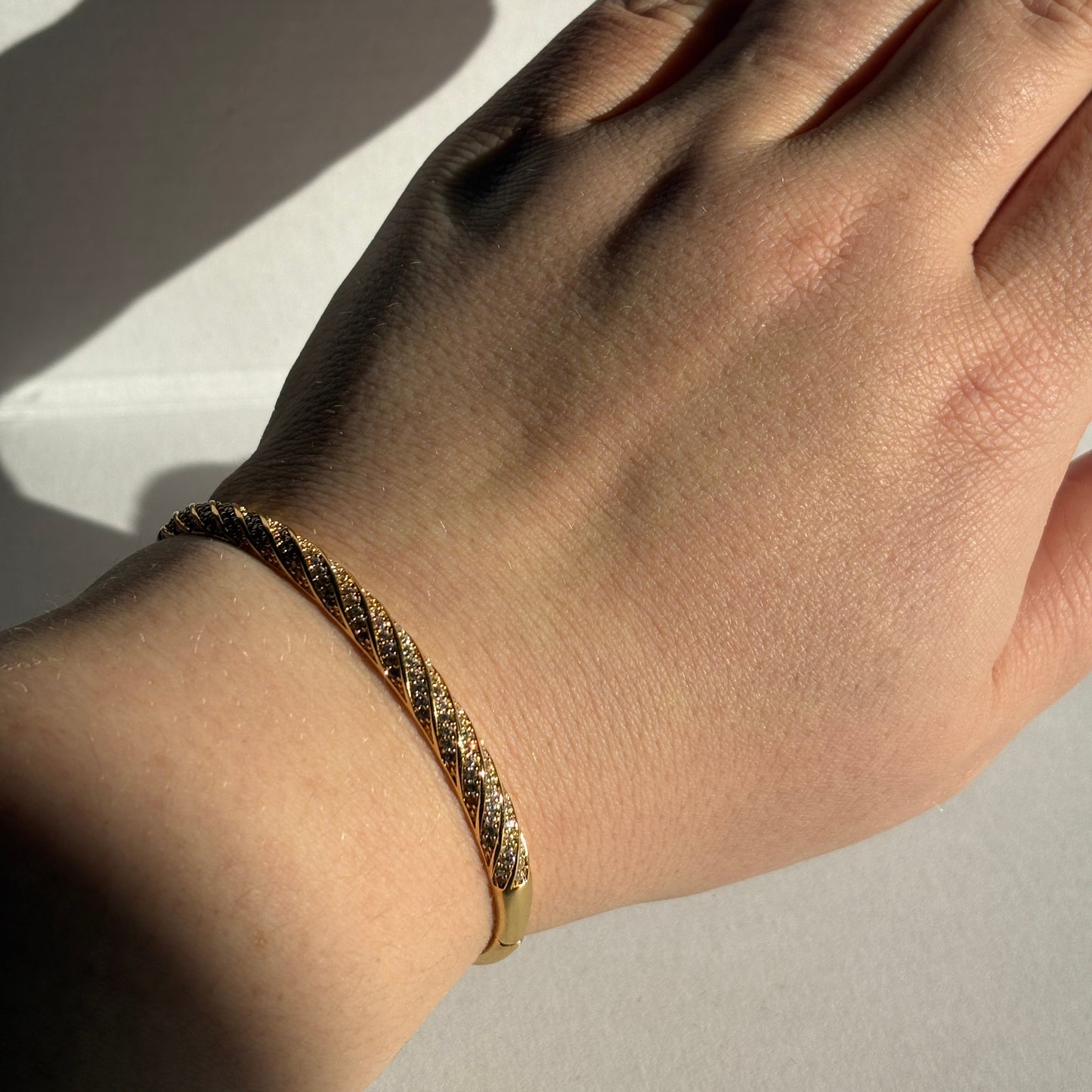 Hand wearing a gold bracelet on a light background

