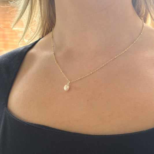 Close-up of a gold necklace with a pendant on a person's neck.

