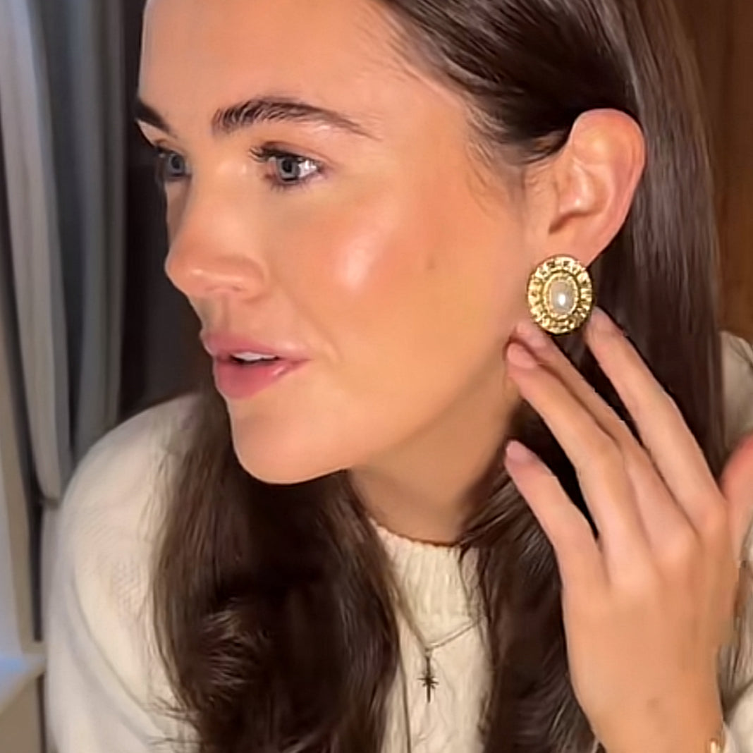 Woman wearing gold earrings, holding hand near ear

