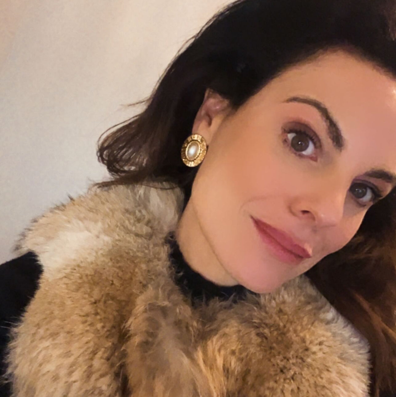 Woman wearing a fur collar and gold earring with a neutral background