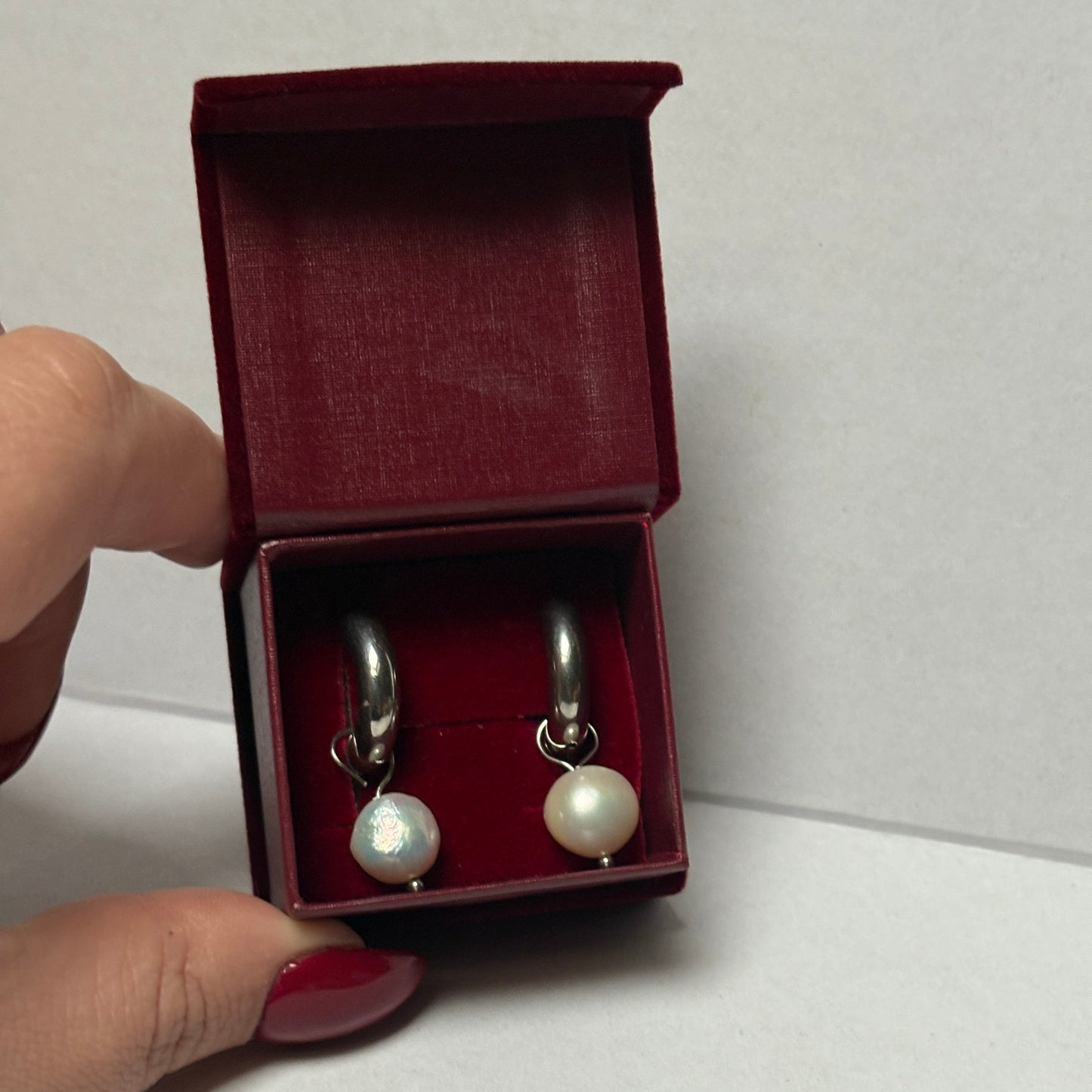 Open jewelry box with pearl earrings held by a hand on a light gray background

