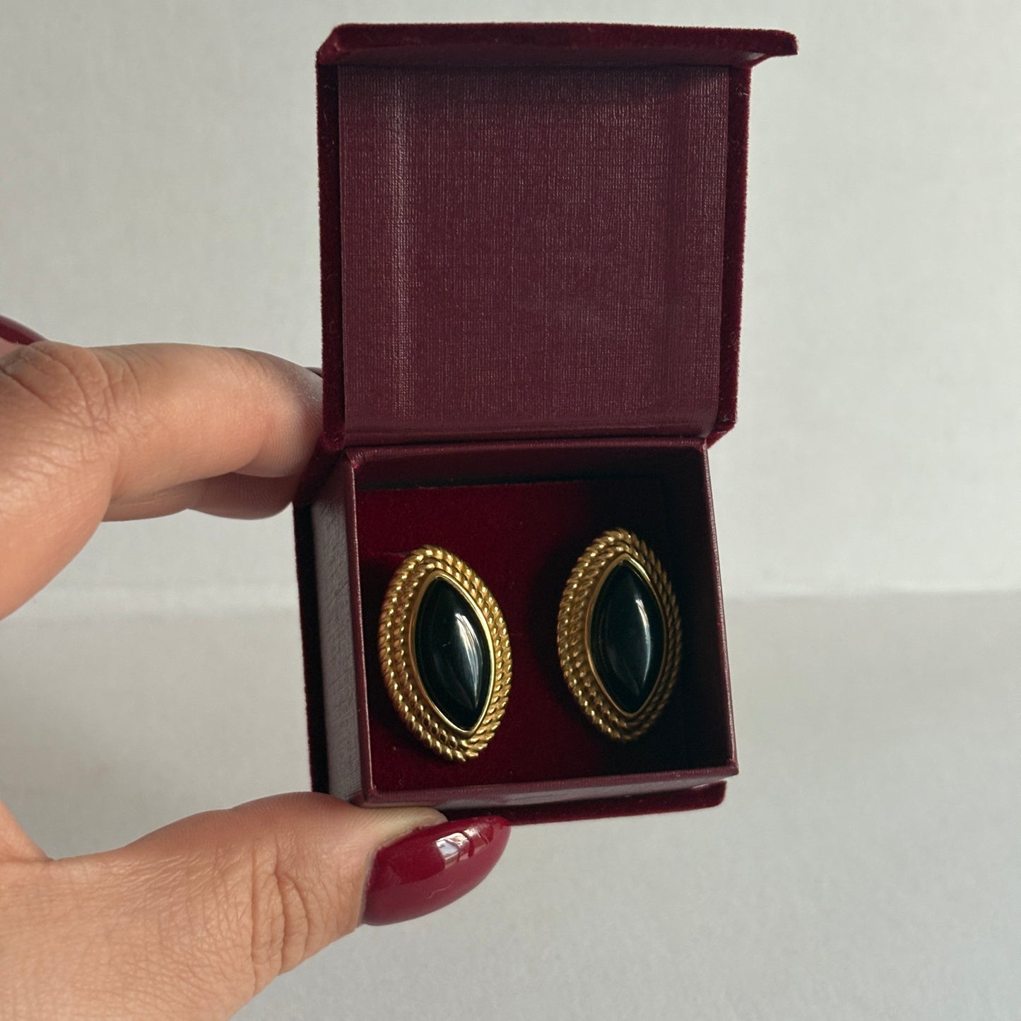Gold and black earrings in a maroon box held by a hand against a plain background
