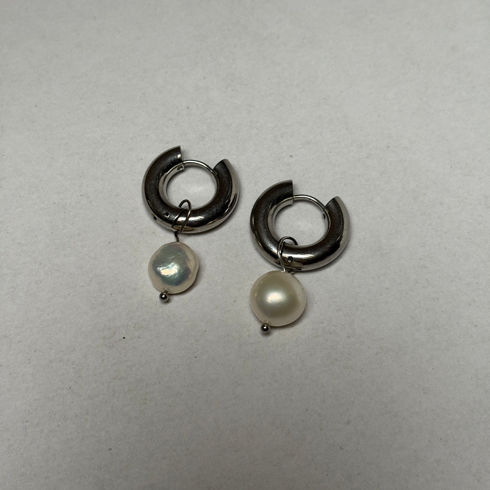 Pair of silver hoop earrings with pearl-like stones on a light gray background
