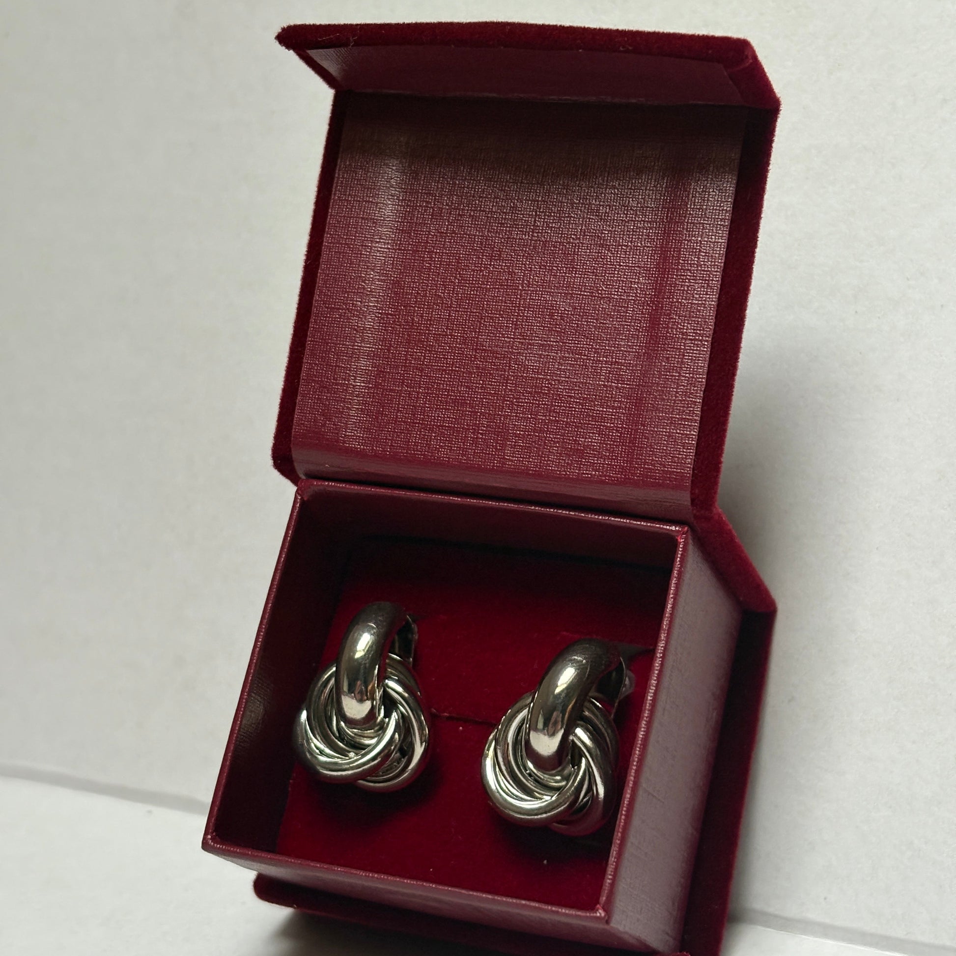 Silver knot-shaped cufflinks in a red box on a light gray background. 