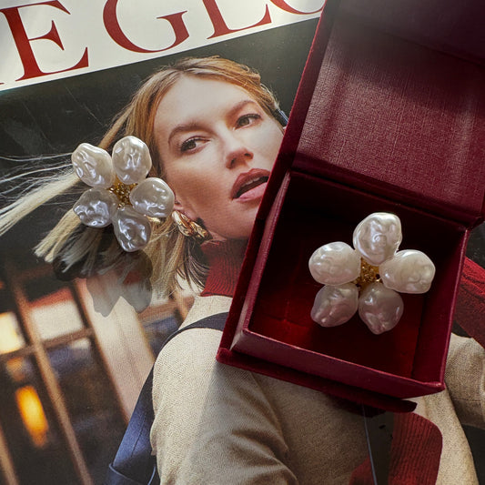 Pearl flower earrings in a red box with a magazine and handbag in the background


