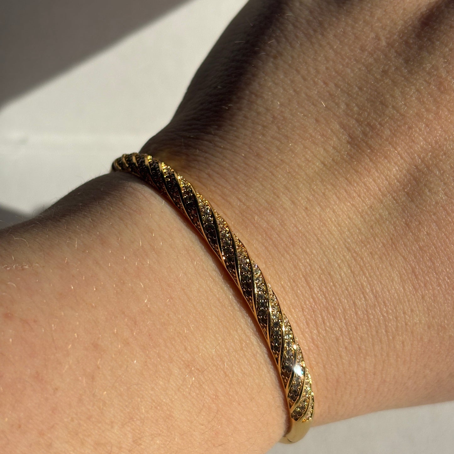 Gold bracelet on a wrist with a neutral background. 