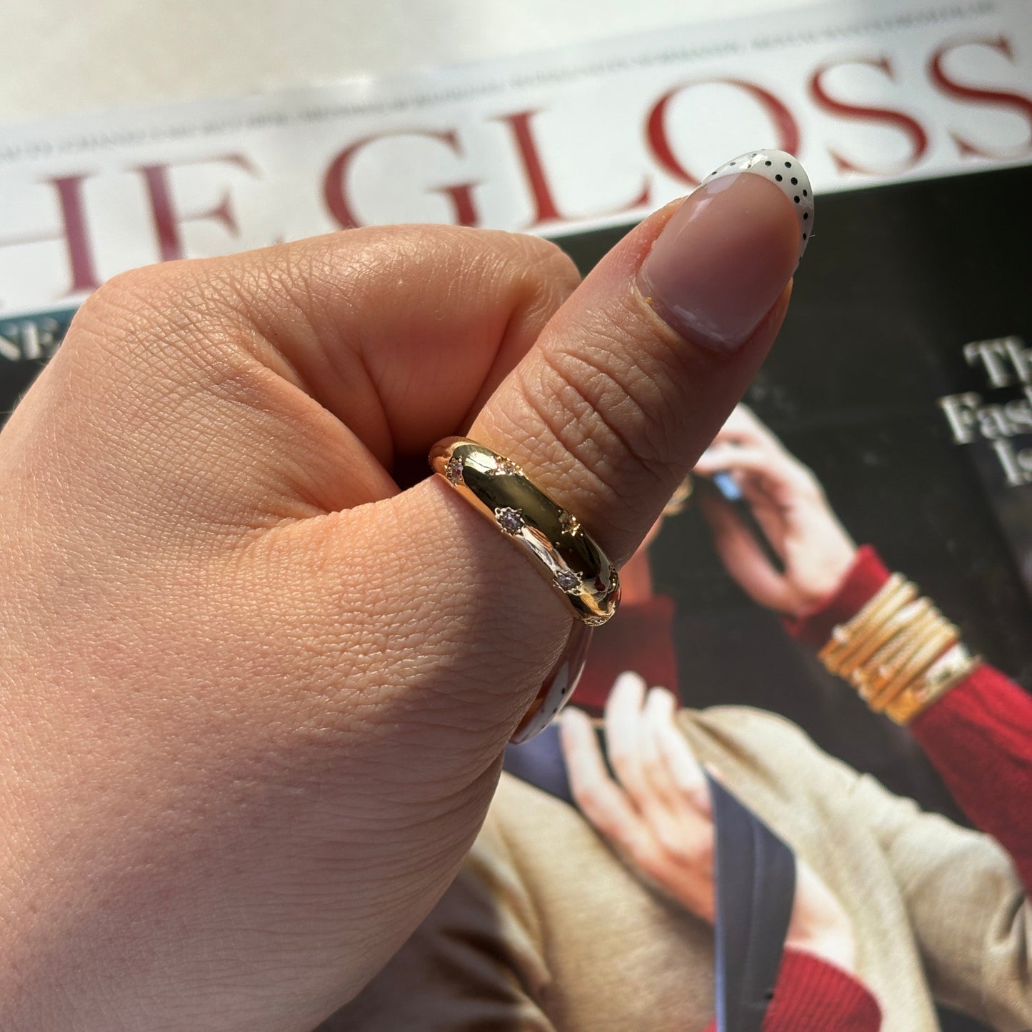Hand wearing a gold ring with a blurred magazine in the background

