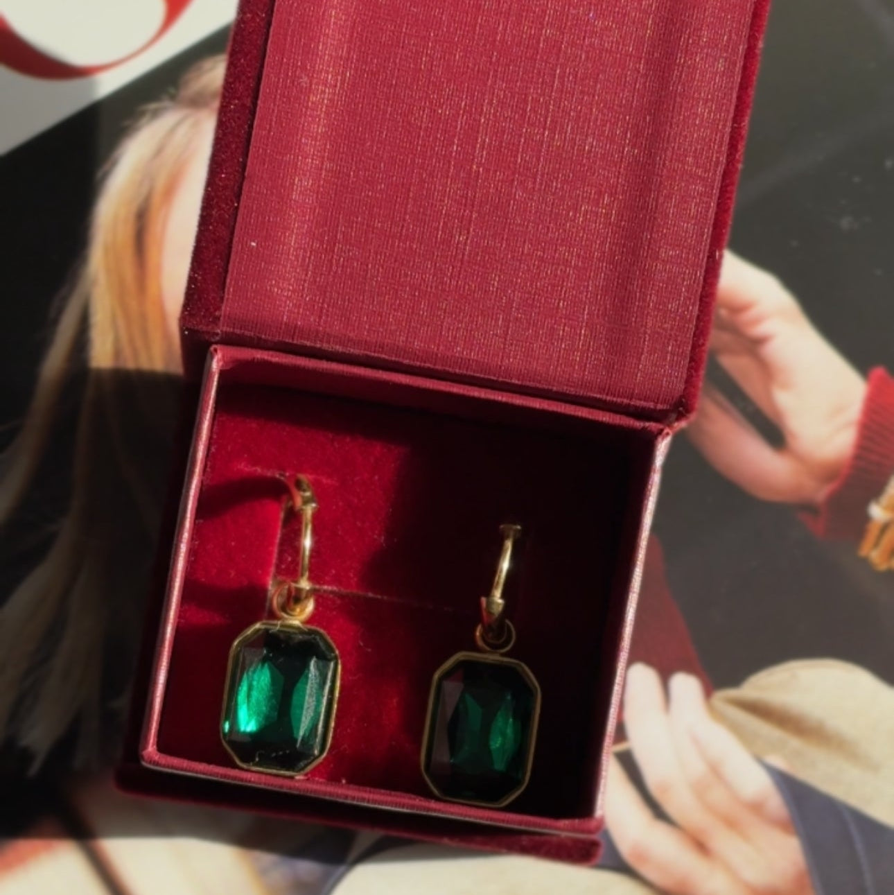 Green emerald earrings in a red jewelry box with blurred background