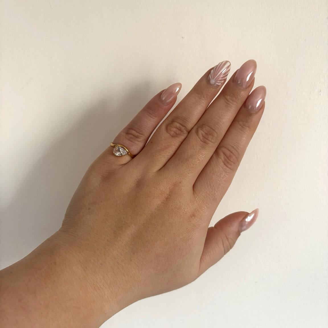 Hand wearing a gold oinky ring with a diamond on a plain background

