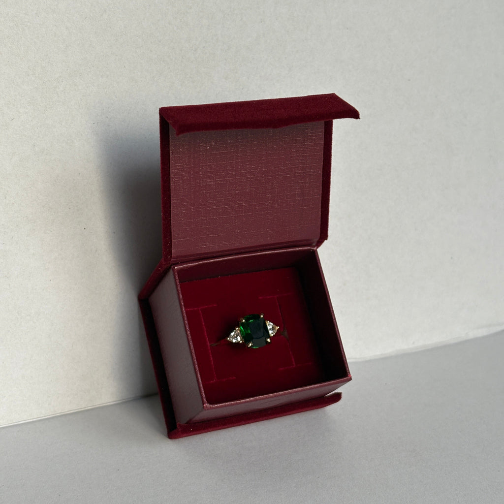 Green gemstone in a red jewelry box on a light gray background


