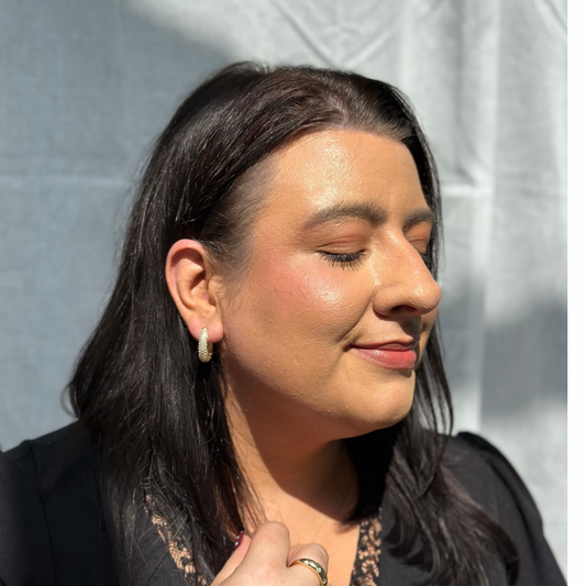 Woman with dark hair and earrings against a light gray background

