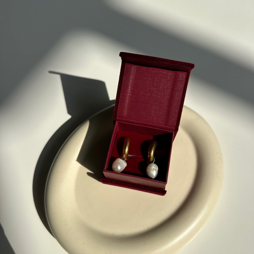 Pair of pearl earrings in a red jewelry box on a reflective surface with soft shadows.