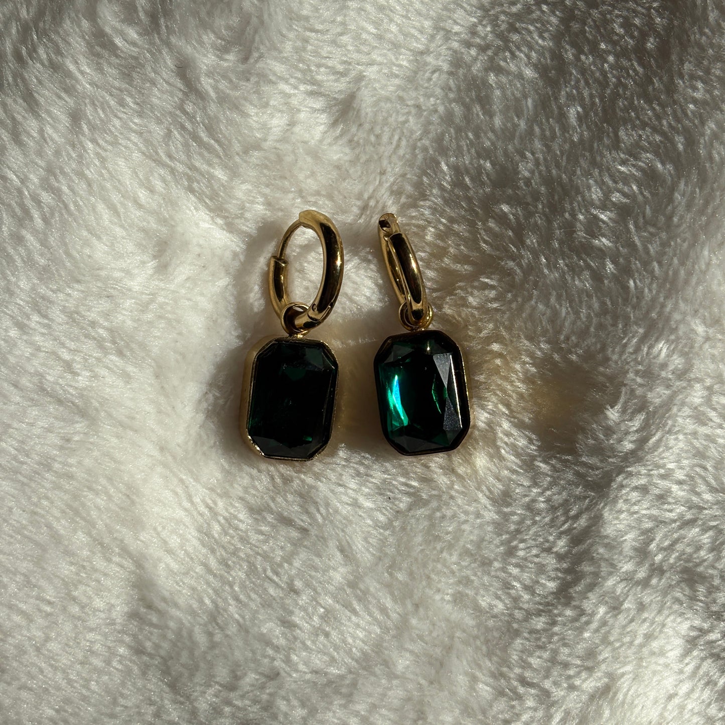 Pair of earrings with green gemstones on a white fur surface

