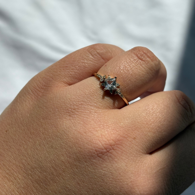 Gold ring with a central diamond and smaller stones on a light fabric background.