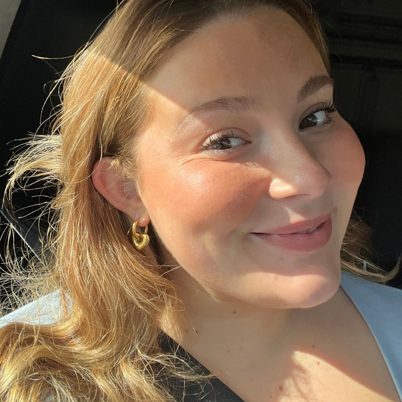 Close-up of a person with blonde hair and a light blue top, wearing a gold earring.

