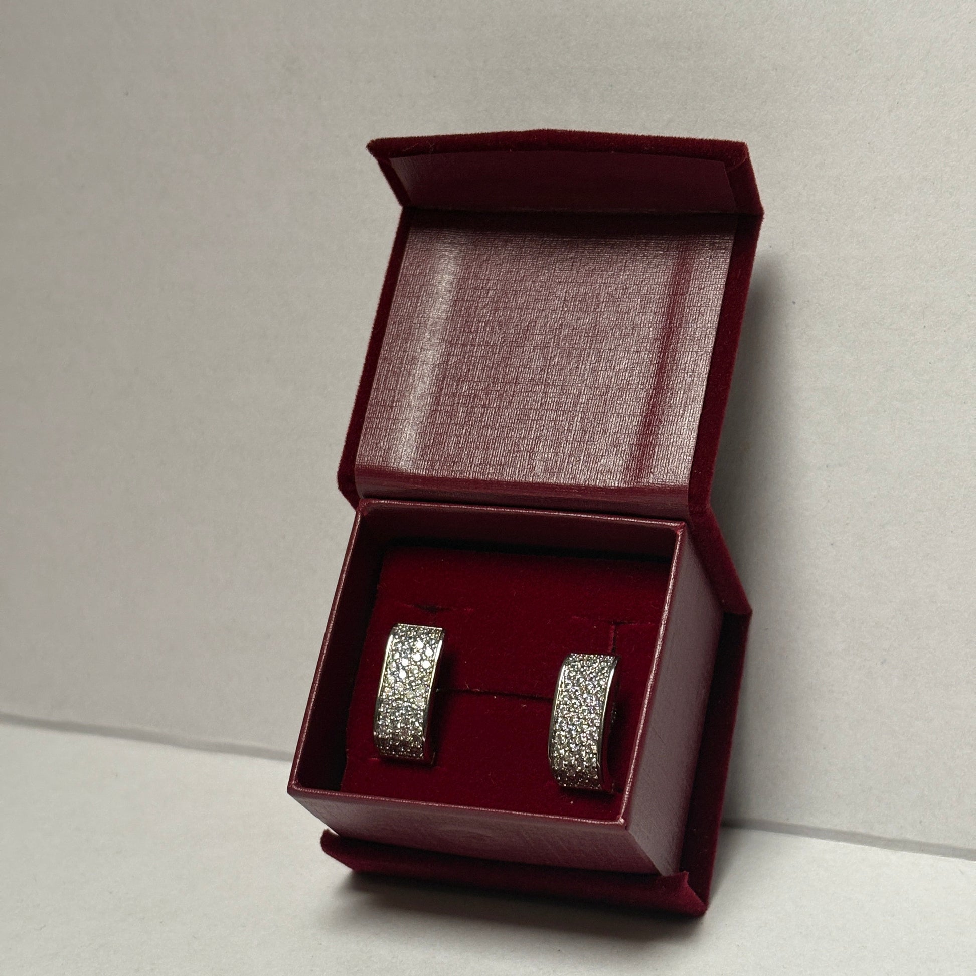 Silver earrings in a maroon jewelry box on a light gray background