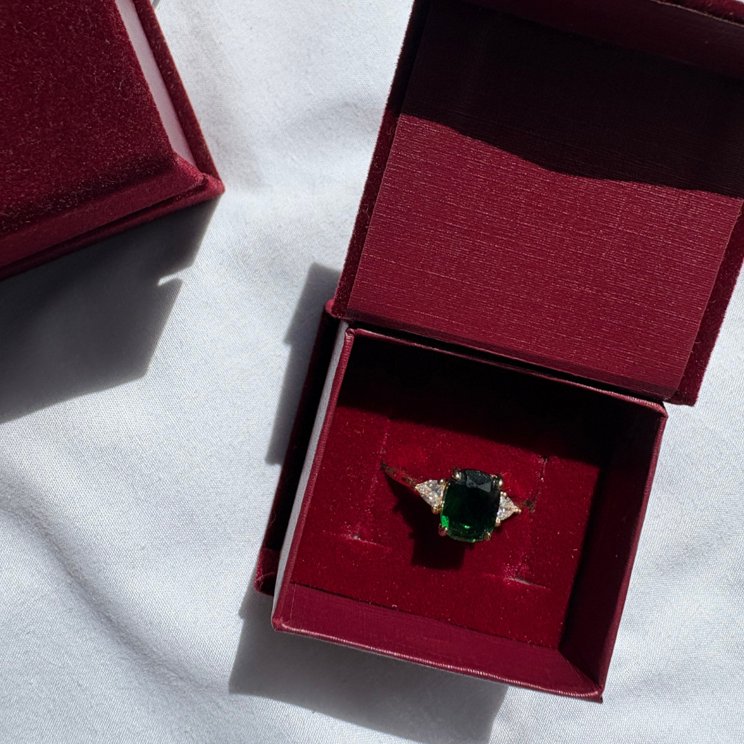 Green gemstone ring in a red velvet box on a white background

