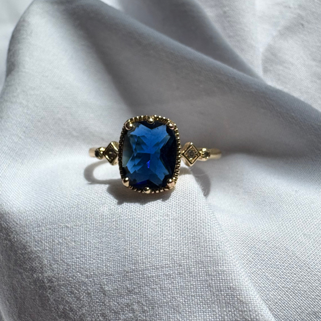 Gold ring with a blue gemstone on a white fabric background

