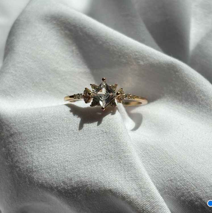 Gold ring with a central diamond and smaller stones on a light fabric background

