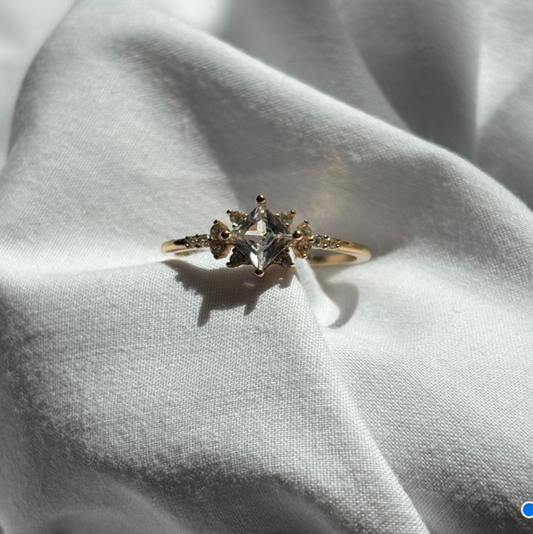Gold ring with a central diamond and smaller stones on a light fabric background

