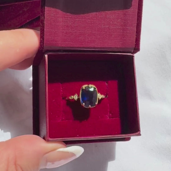 Gold ring with a blue gemstone in a burgundy box.

