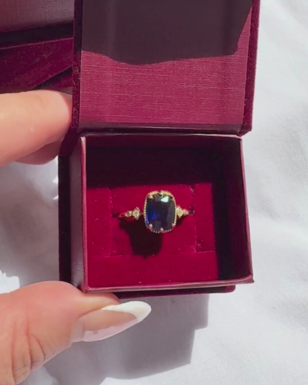Gold ring with a blue gemstone in a burgundy box.

