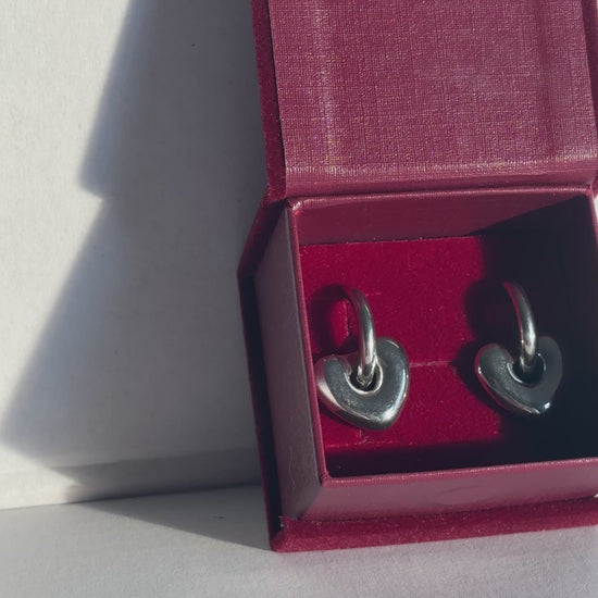 Red jewelry box with silver earrings on a light gray background. 