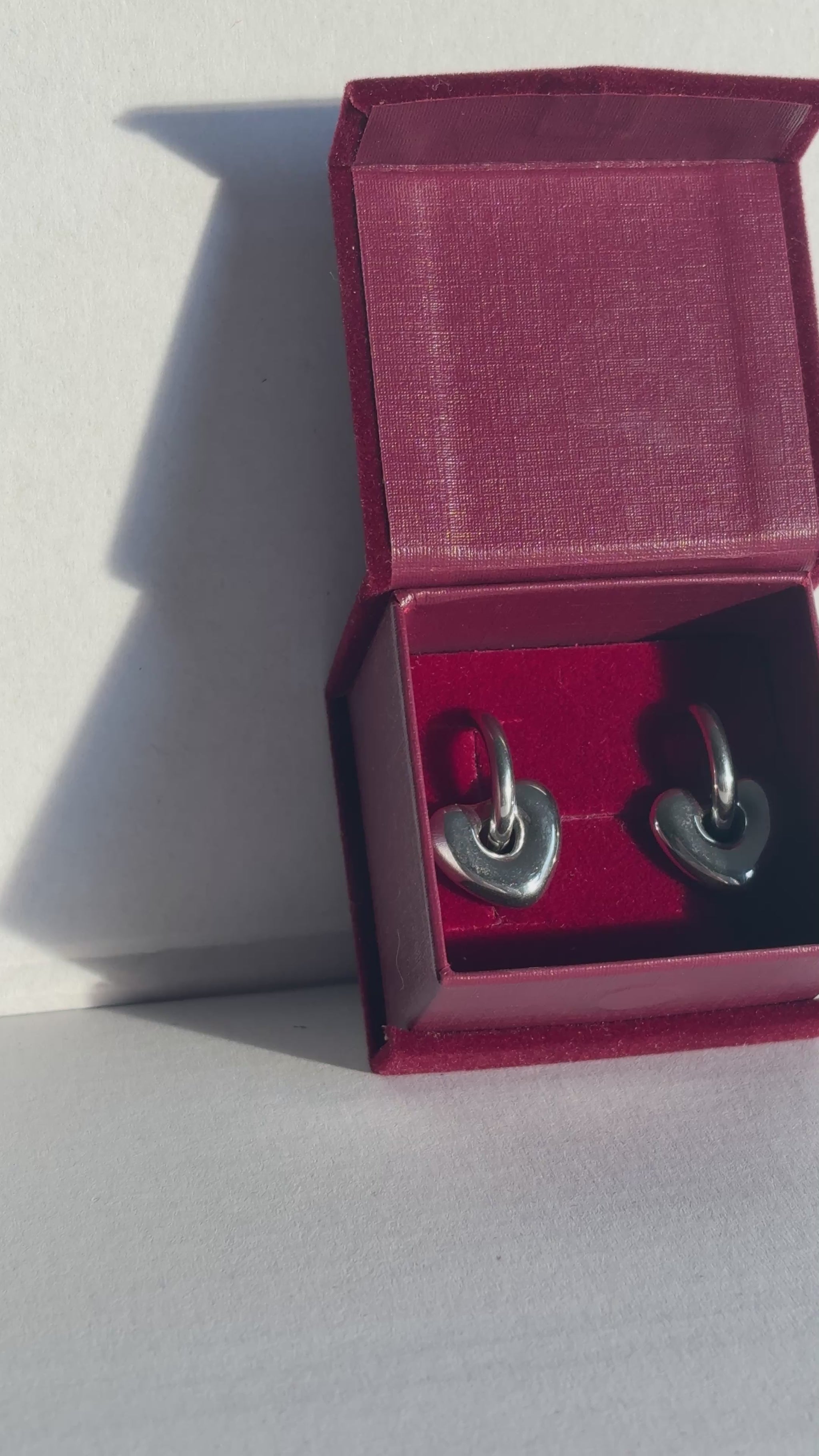 Red jewelry box with silver earrings on a light gray background. 