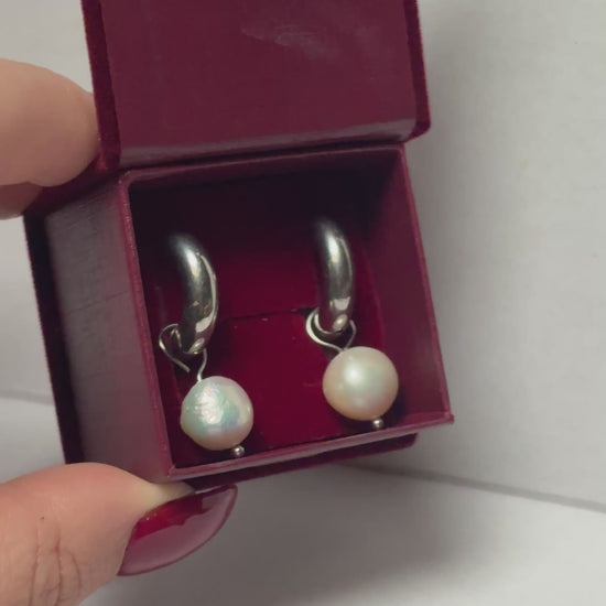 Open jewelry box with pearl earrings held by a hand on a light gray background